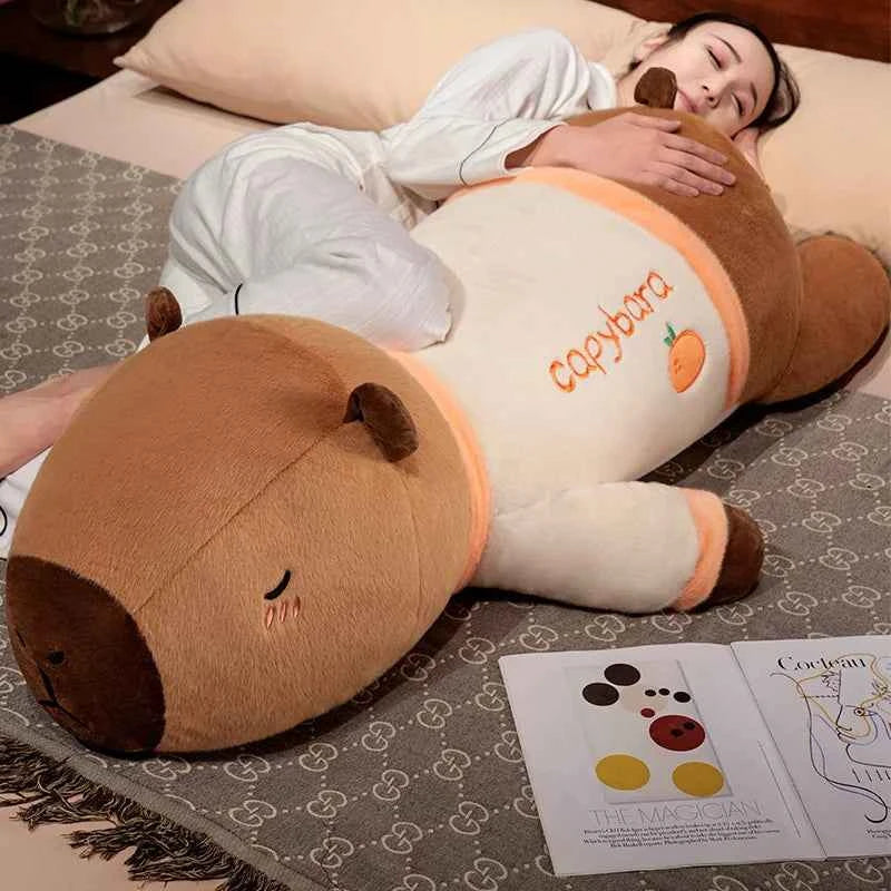 A giant 100cm Kawaii capybara plush toy with small wings in a lying position, used as a cozy body pillow on a modern sofa.