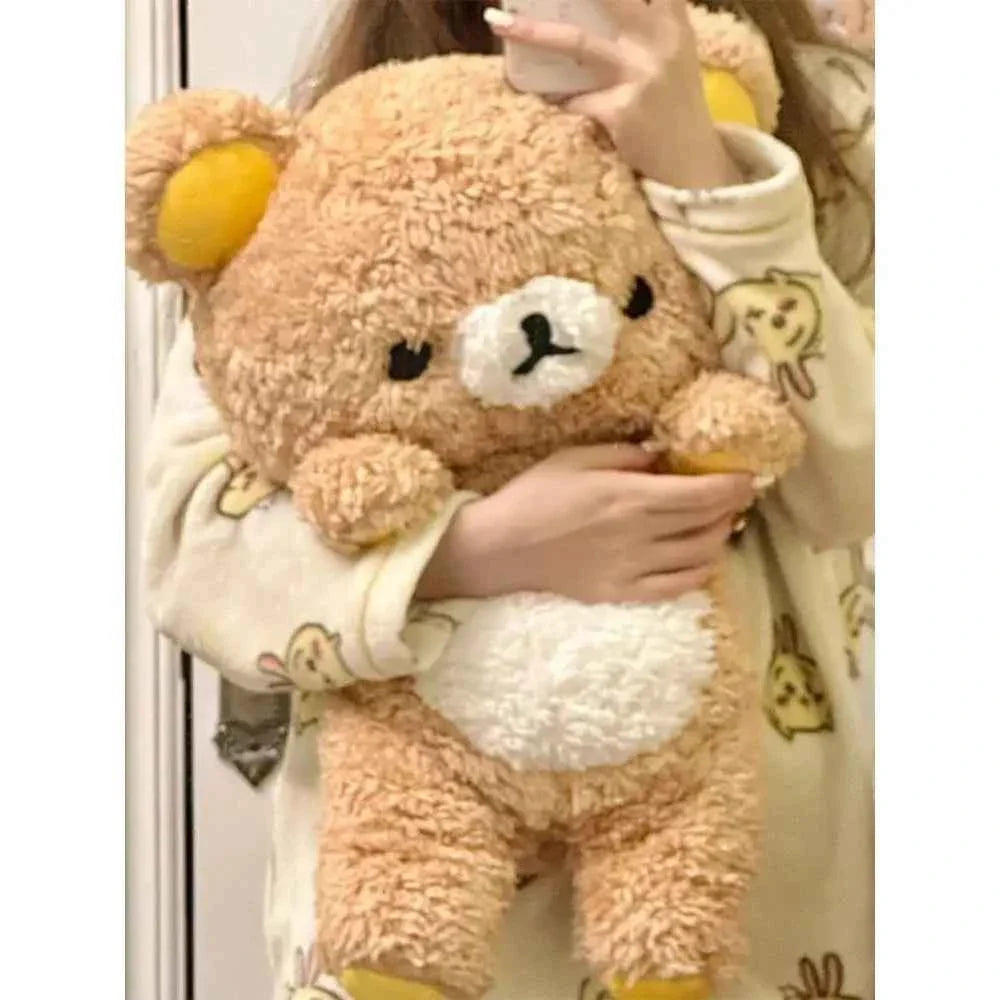 A giant 80cm Rilakkuma plush toy sitting on a bed, showcasing its soft brown fur, iconic yellow ear accents, and a large huggable size.