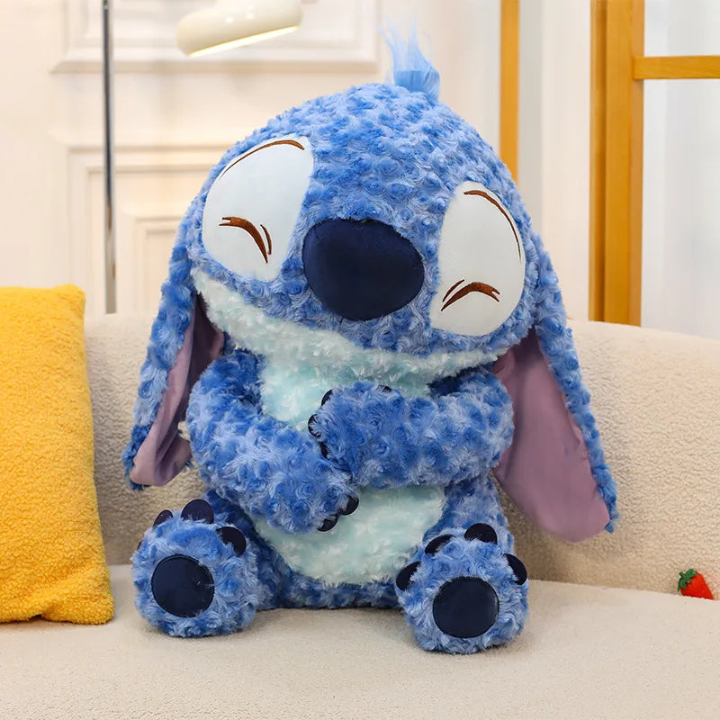 A variety of blue Stitch plush toys in different sizes and poses, featuring large ears and alien features, alongside Angel and Scrump soft toys on a bright background.