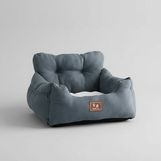 Dark gray pet bed on a white surface with a vase of flowers and teddy bear in the background.
