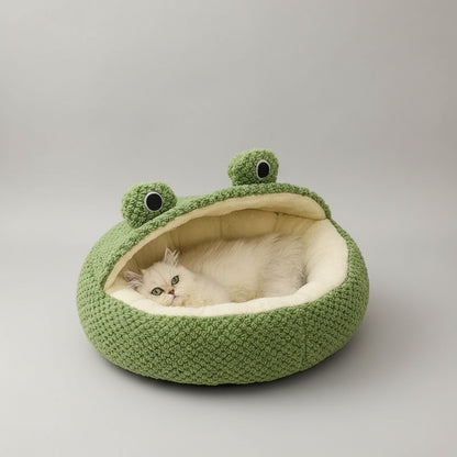 Green frog-shaped pet bed with a white cat inside on a light wooden floor.