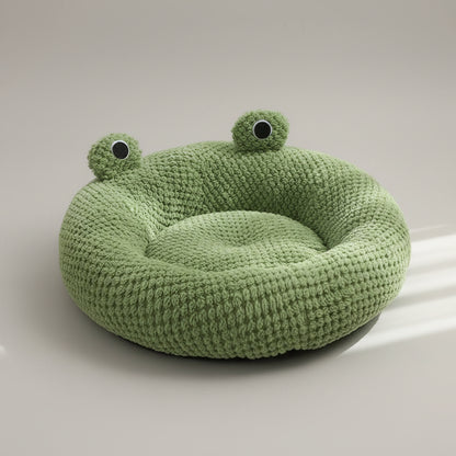 Green frog-shaped pet bed with a white cat inside on a wooden floor.